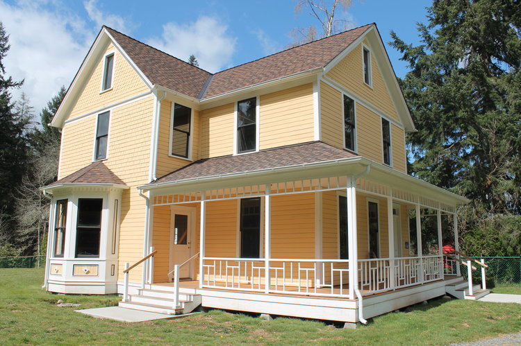 The Reard Freed House exterior after restoration work. It is yellow with white trim, has a bay window, and a partial wrap-around porch.