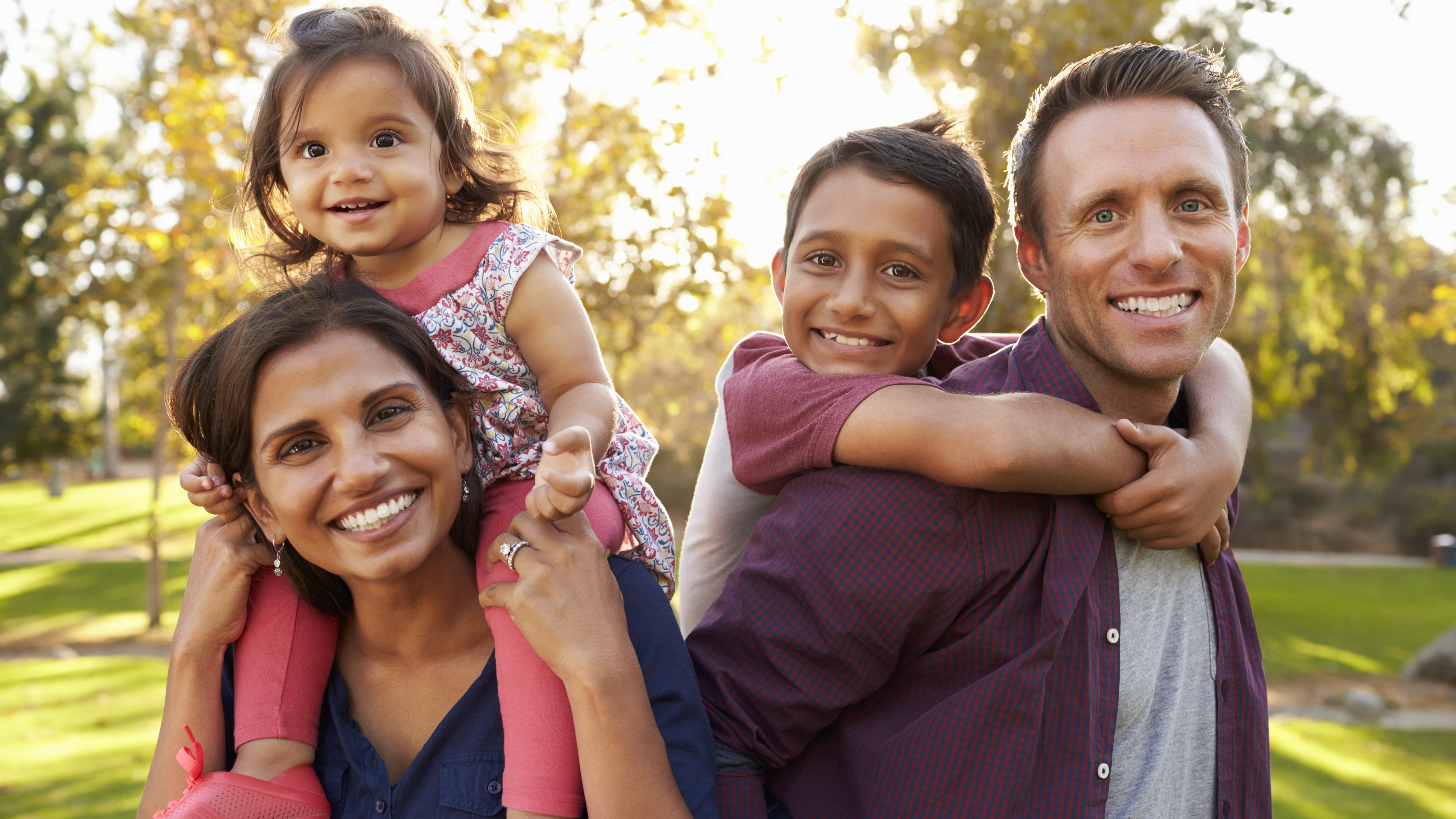 A woman with a female toddler on her shoulders and a man giving a boy a piggy-back ride. 